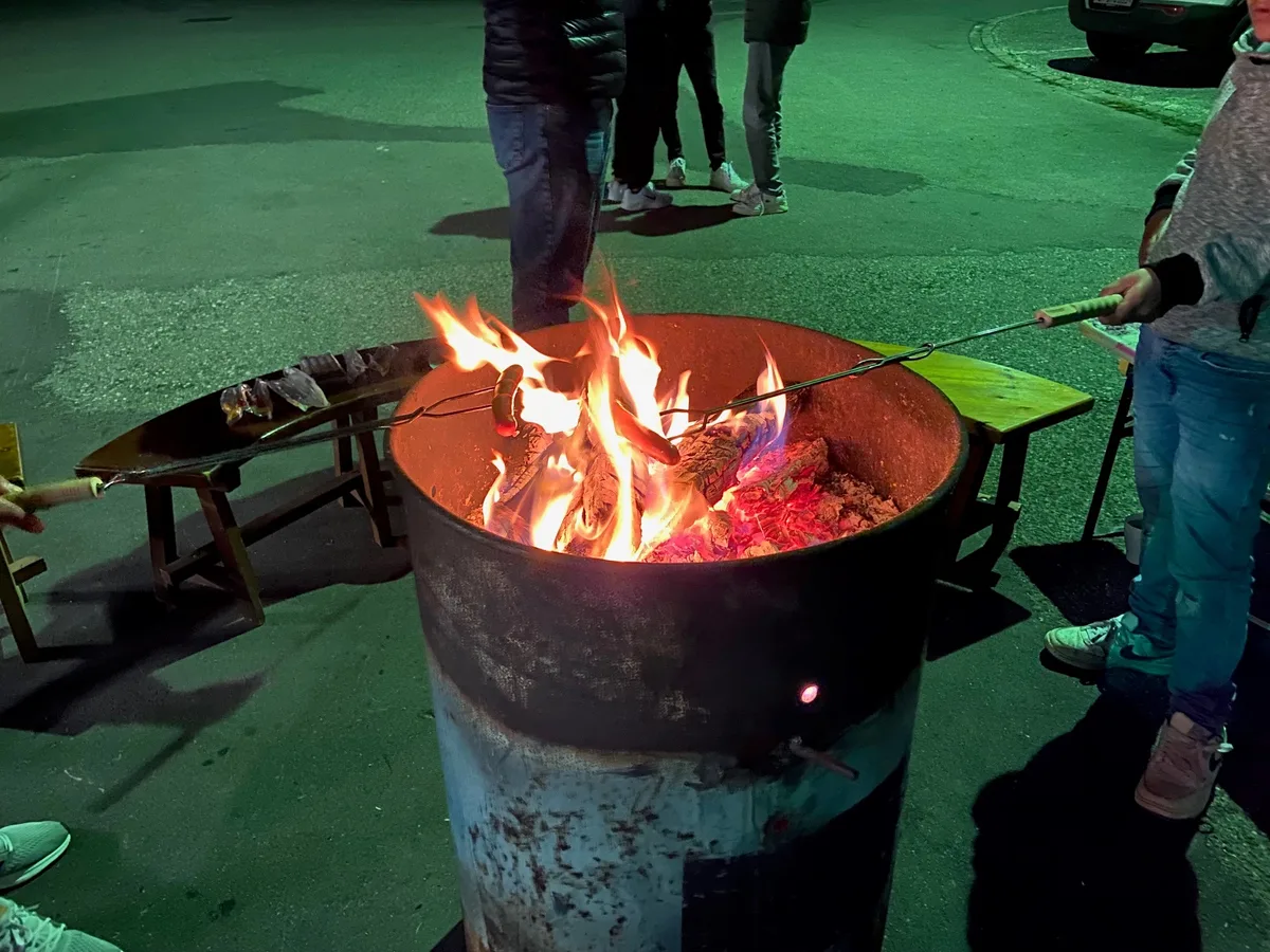 Am Ende des Abends werden Poulet-Würstchen über dem Feuer gebraten. Eine Feuertonne und Menschen, die Würstchen braten.
